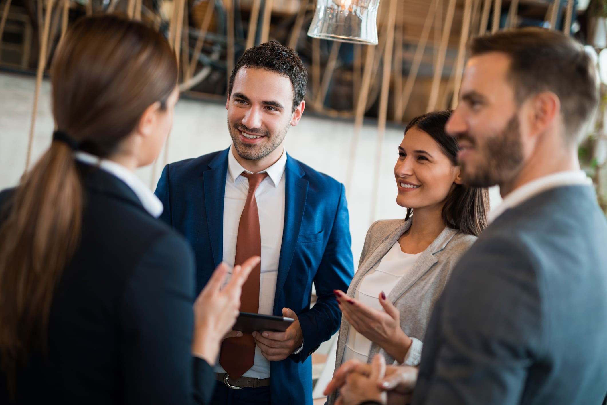 Four young business people are discussing business strategy in the office building hallway using digital tablet and reviewing data. Focus on background.